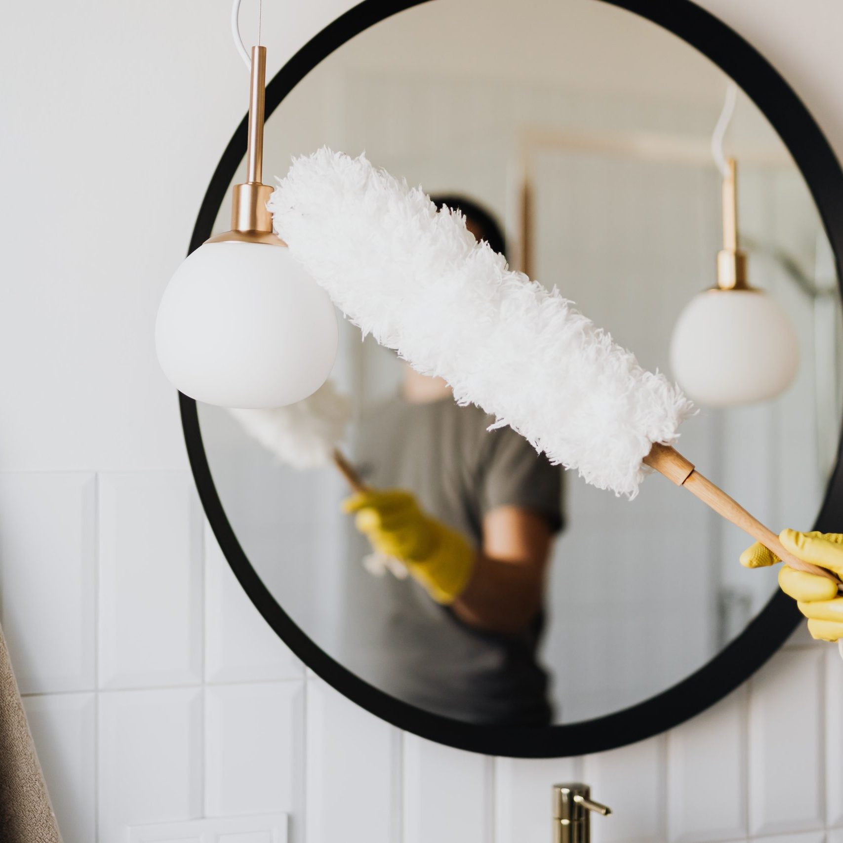 Photo of cleaner dusting a mirror in bathroom